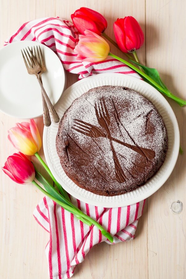 Chocolate torte cake dusted with powdered sugar making two forks pattern next to tulips.