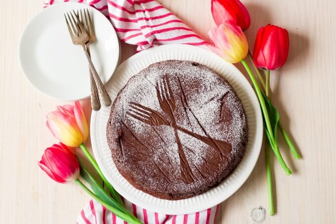 Chocolate torte cake dusted with powdered sugar making two forks pattern next to tulips.