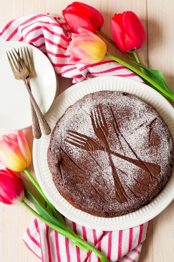 Chocolate torte cake dusted with powdered sugar making two forks pattern next to tulips.