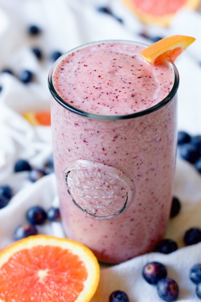 Pink smoothie in a glass with fresh blueberries and orange slices.