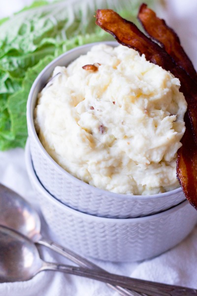 Mashed potatoes in two stacked bowls with crispy bacon and green cabbage.