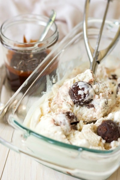 Homemade ice cream in a glass loaf pan with brownies mixed in and chocolate fudge sauce in a jar on the side.