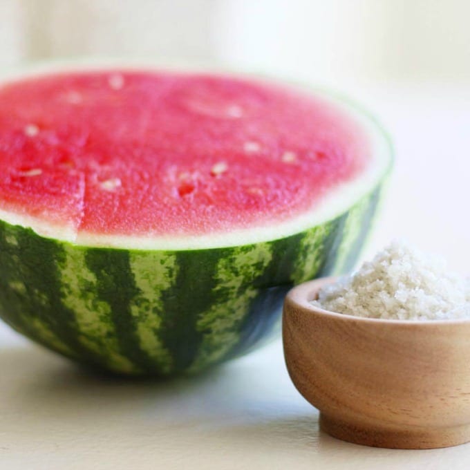 Half of a fresh watermelon and a bowl of sea salt.