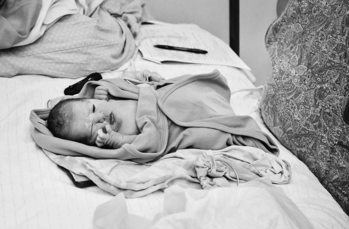 Newborn baby having his newborn exam on a bed at home with his midwife.