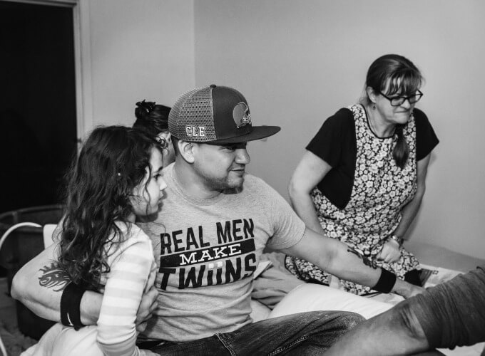 A husband of twins watching his wife in active labor during a home birth surrounded by the birth team.