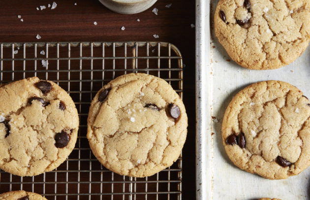 chocolate chip cookies sit on a cooling rack and tray with a bowl of salt nearby