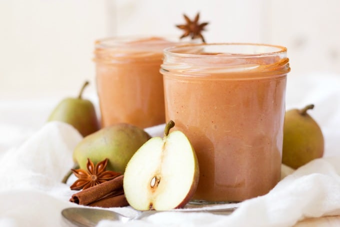 Jars of homemade applesauce surrounded by pears, cinnamon sticks and star anise pods.