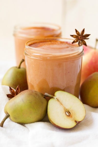 Jars of homemade applesauce surrounded by pears and star anise pods.