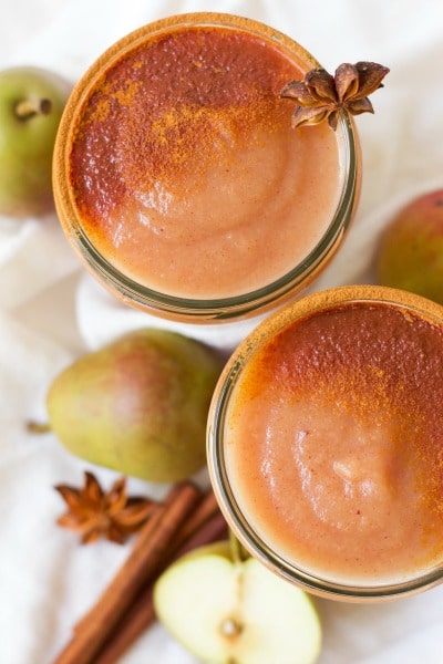 Jars of homemade applesauce dusted with cinnamon surrounded by whole pears, cinnamon sticks and star anise pods.