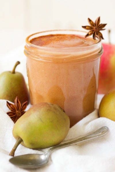 Jar of homemade applesauce dusted with cinnamon surrounded by whole pears and star anise pods.