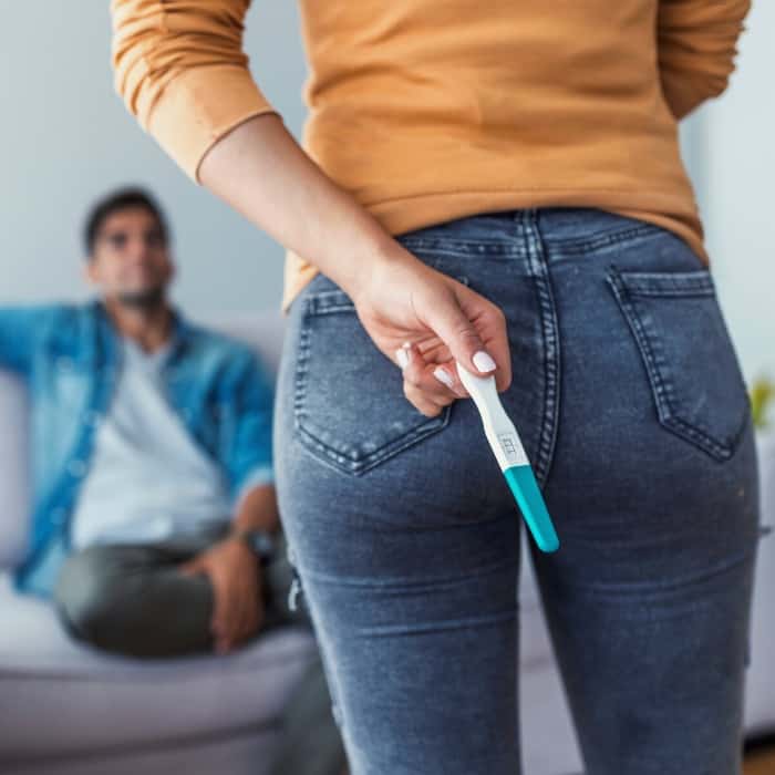 woman holding a positive pregnancy test behind her back