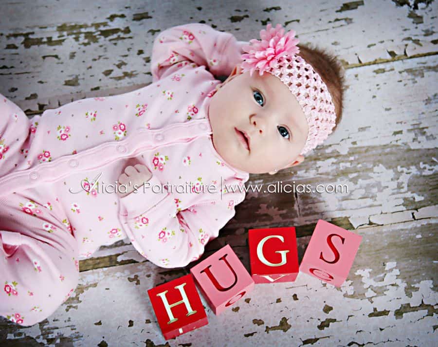 Baby laying on floor next to pink and red blocks spelling out Hugs