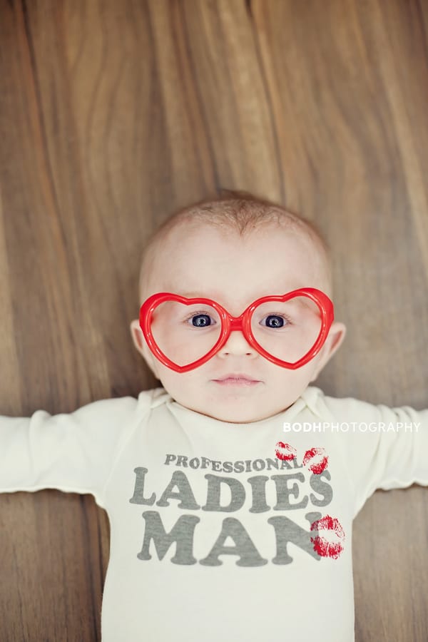 Baby laying on floor wearing red heart shaped glasses