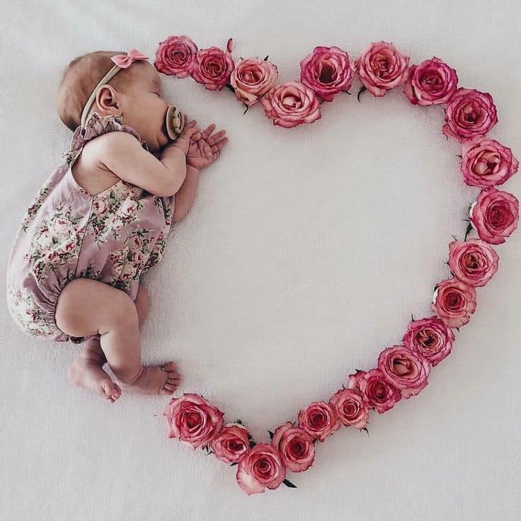 Sleeping baby laying next to heart made out of pink roses