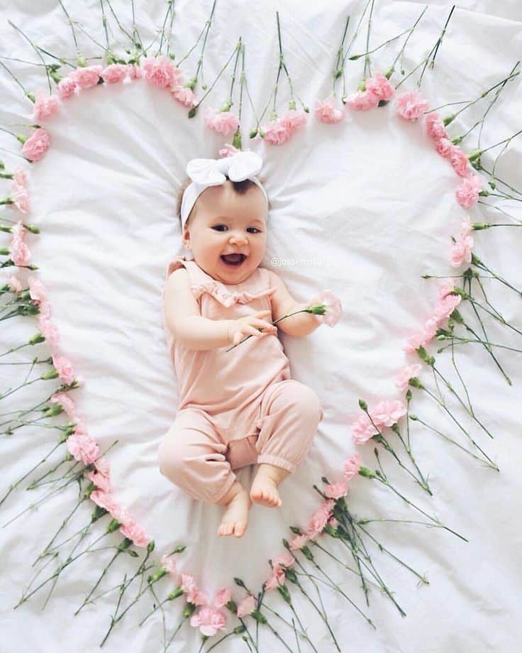 Laughing baby laying on bed surrounded by pink carnations