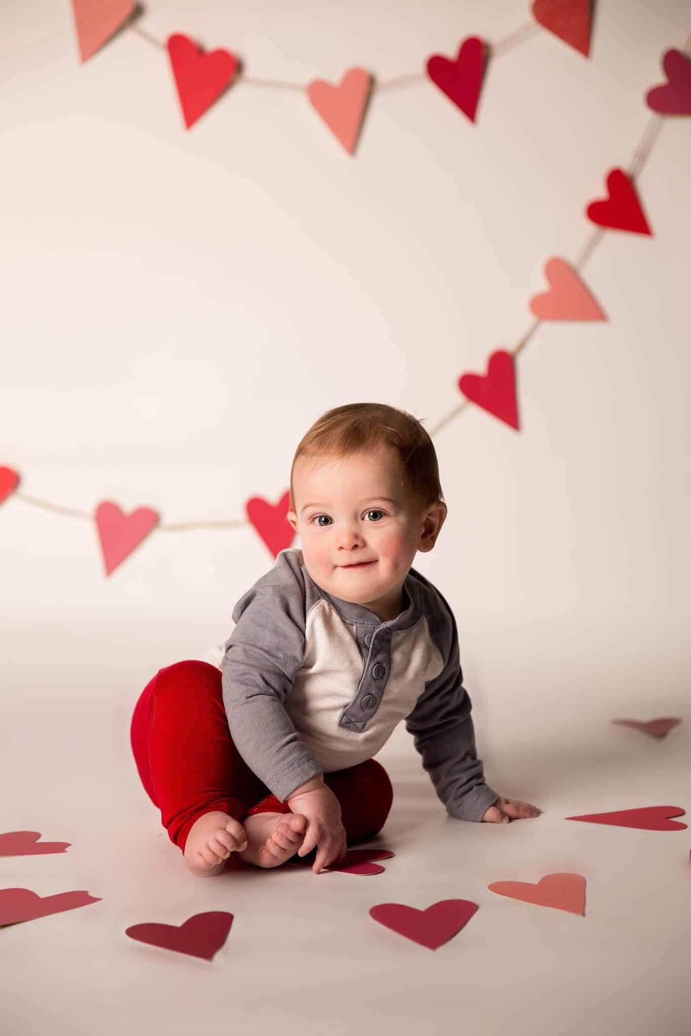 baby sitting on floor surrounded by hearts for Baby's First Valentine's Day Photo shoot