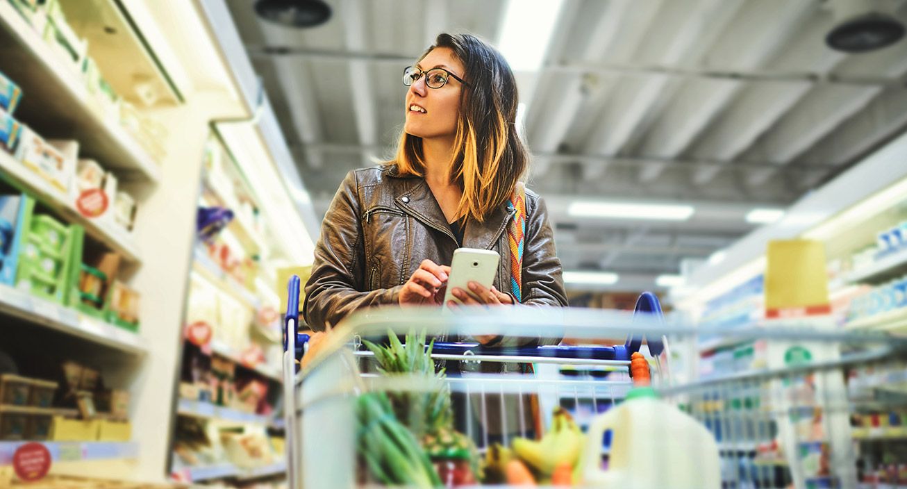 A girl at the grocery store looking at a list on her phone. 