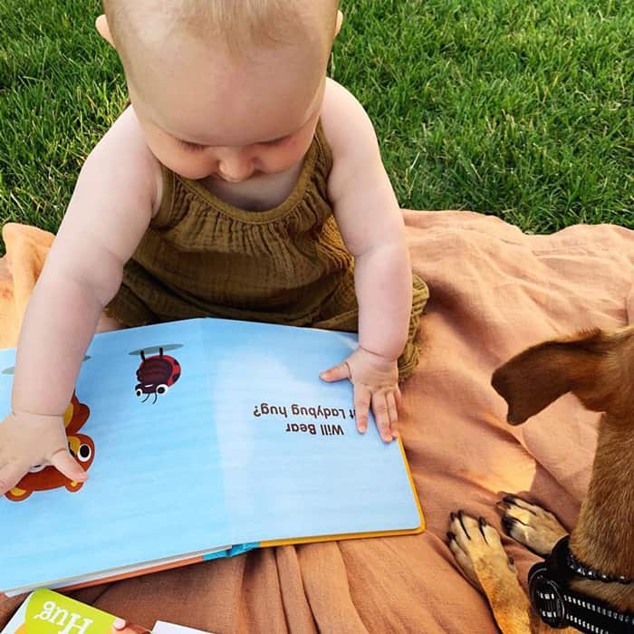 Baby sitting on a blanket in the grass reading Will Ladybug Hug?