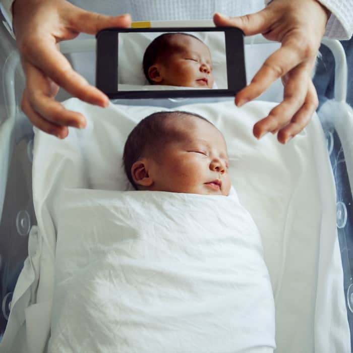 holding a smartphone while taking a picture of a newborn leap year baby