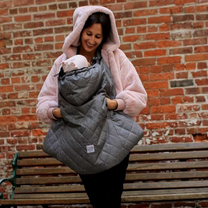 woman outside carrying baby with a carrier cover