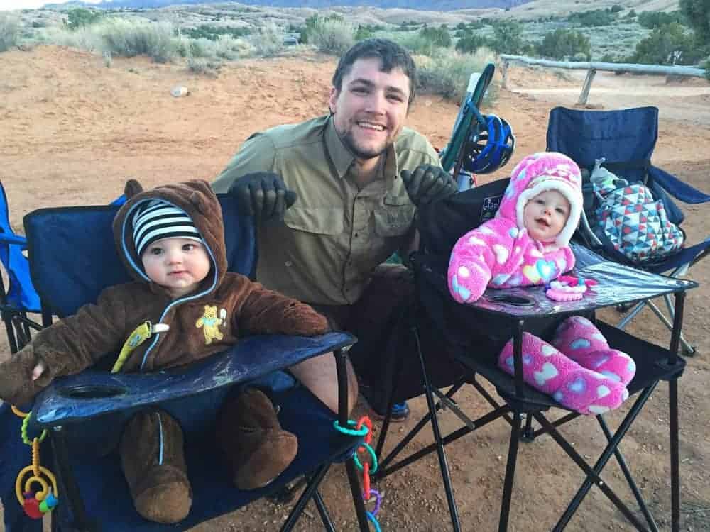 two kids in portable high chairs camping with dad