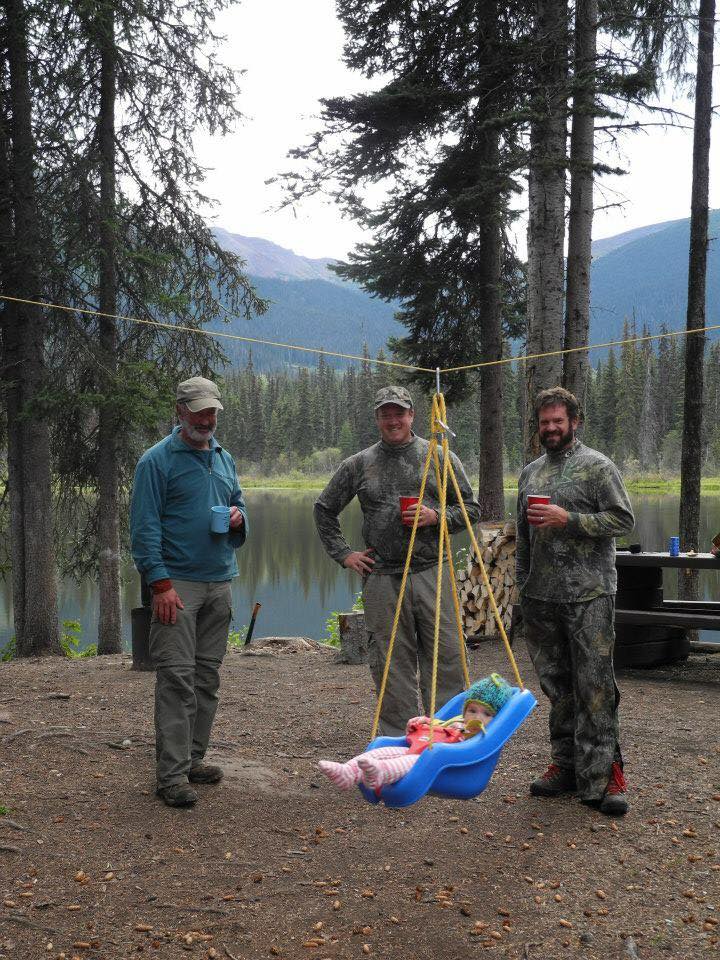 three men camping with a baby in a baby swing