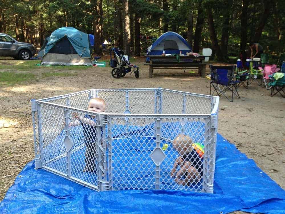 two babies camping in a playard with a tarp underneath