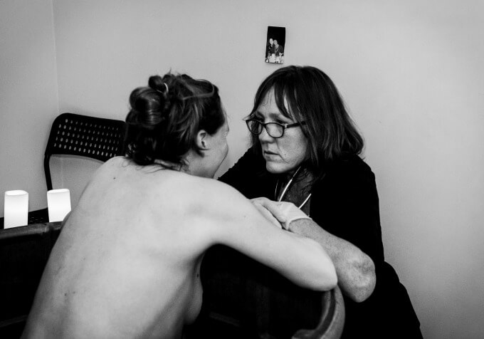 A mother in active labor in a birthing tub during a water birth home birth looking at her midwife.