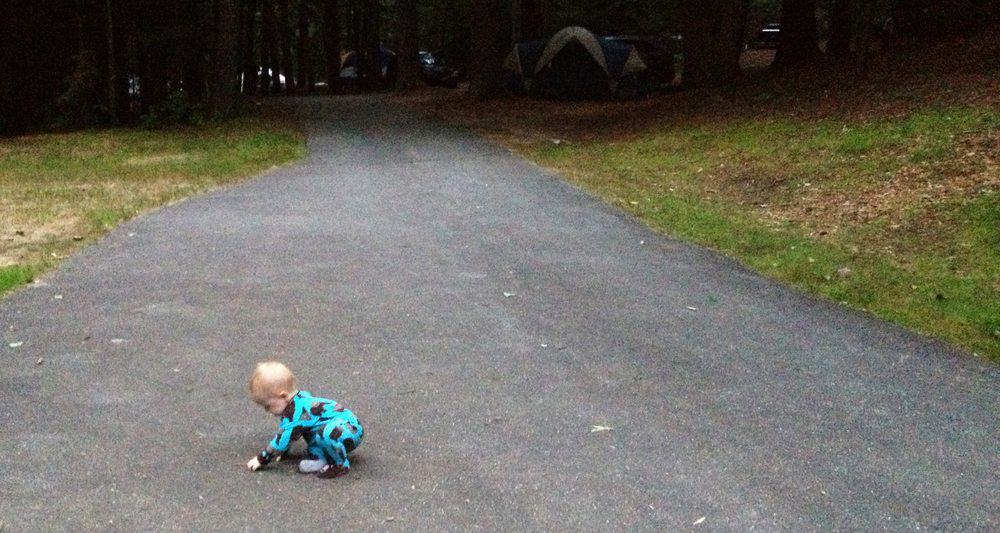 baby in sleepers picking rocks off the road while camping